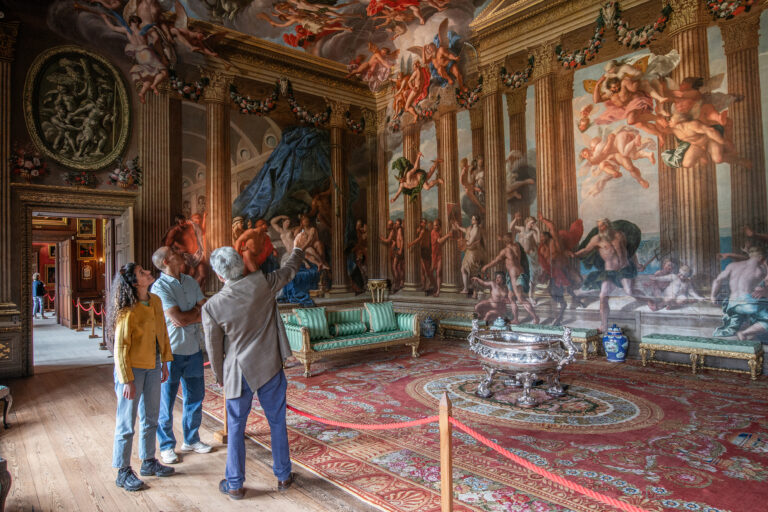 A tour guide describing paintings to a man and a woman inside Burghley House, near Stamford.